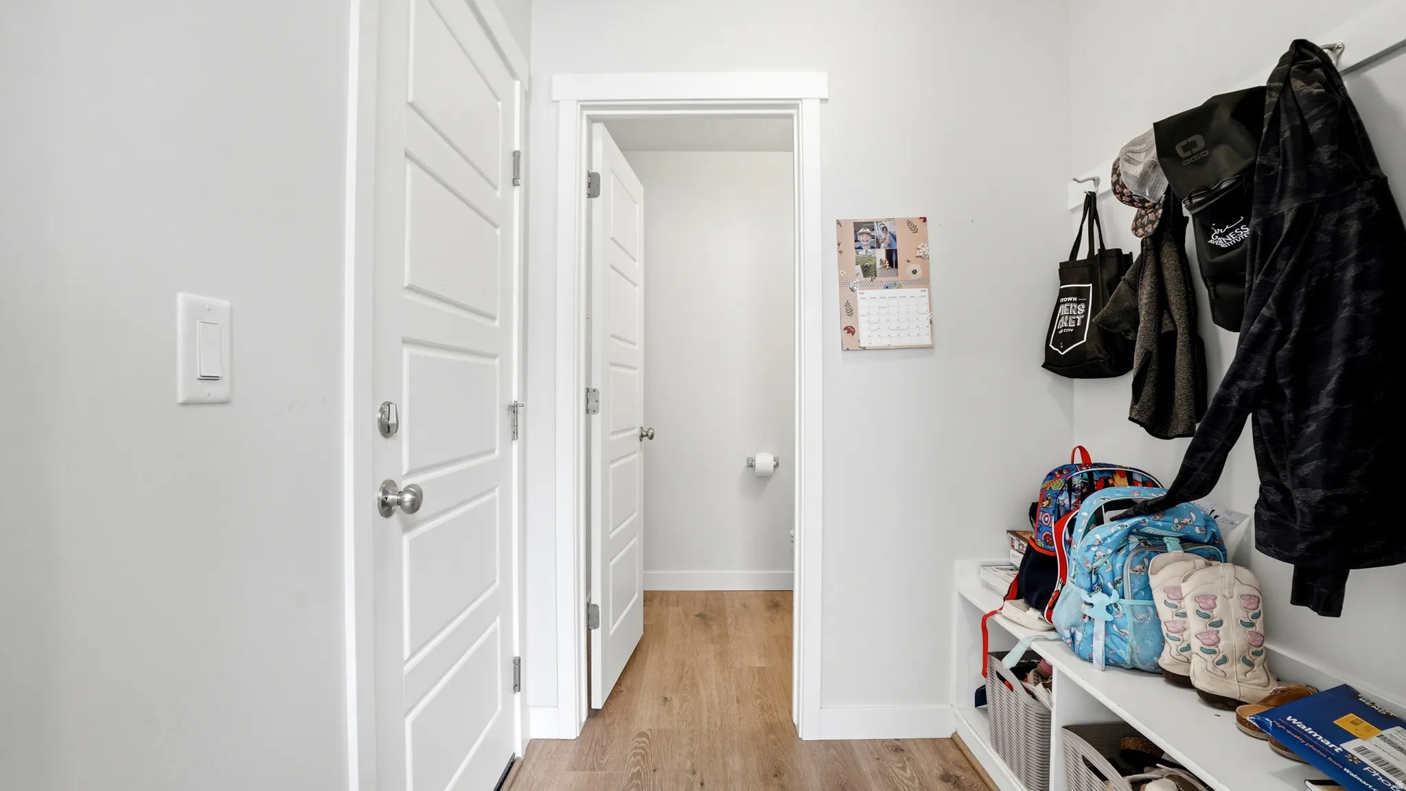 Entryway featuring wood-finish flooring, white trim, and a built-in storage bench with coat hooks