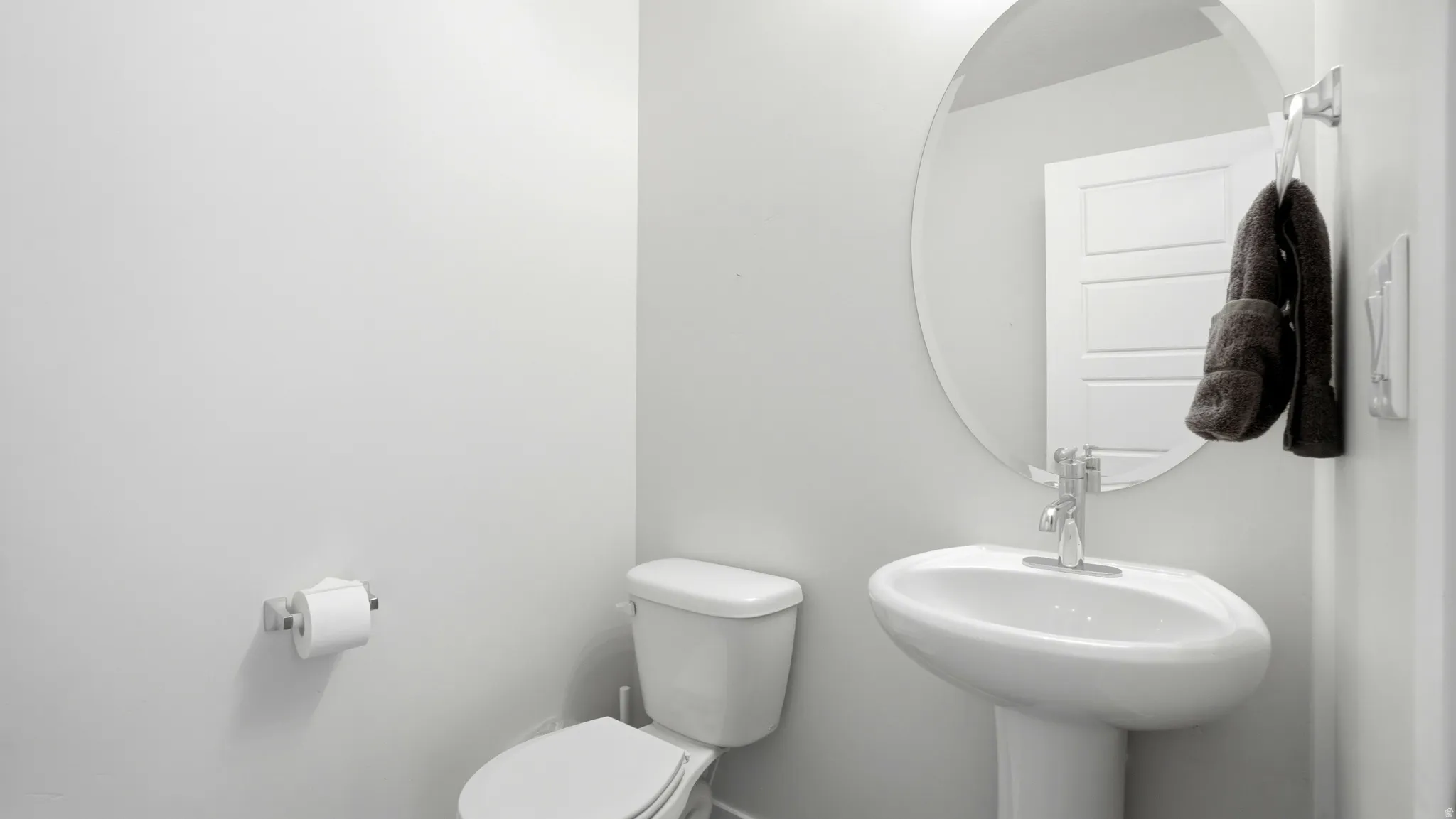 Pedestal sink with a polished chrome faucet, round wall-mounted mirror, and white panel door