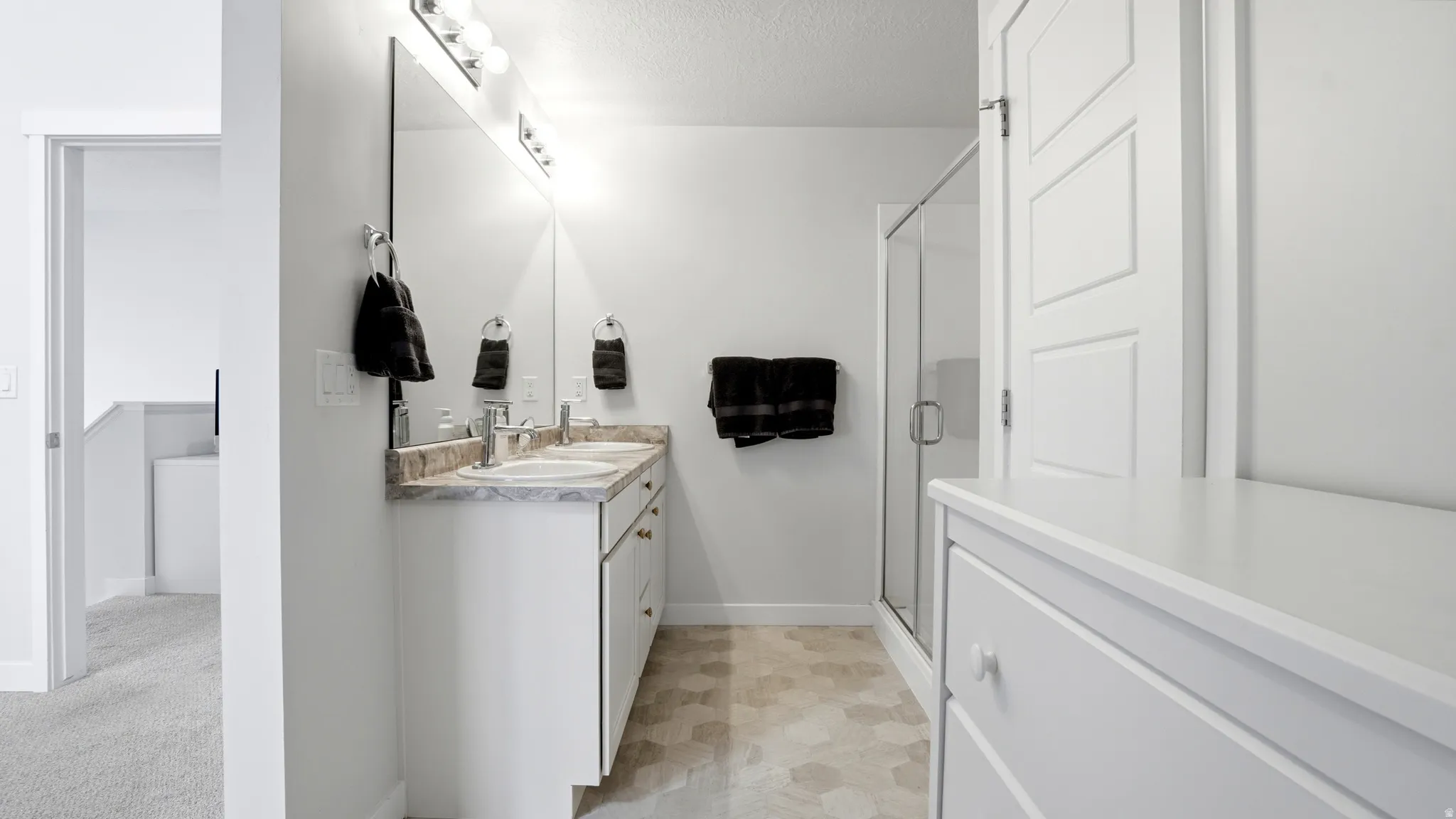 Bathroom featuring a double vanity with two undermount sinks, a large wall mirror, and a glass-enclosed shower