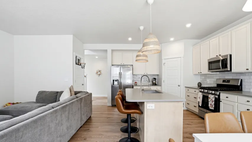 Open-concept kitchen featuring white shaker cabinetry, stainless steel appliances, a light-toned island with integrated sink, and wood-finish flooring