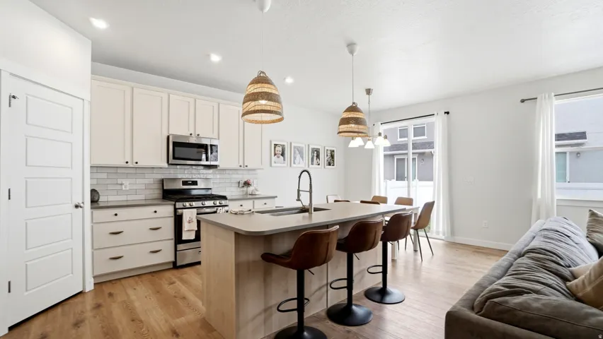 Open-concept kitchen featuring light-toned cabinetry, stainless steel appliances, a subway tile backsplash, and a large island with integrated seating