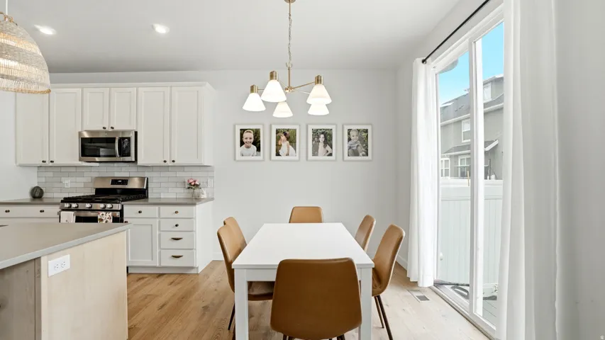 Dining area and kitchen featuring wood-finish flooring, white cabinetry, stainless steel appliances, and a subway tile backsplash