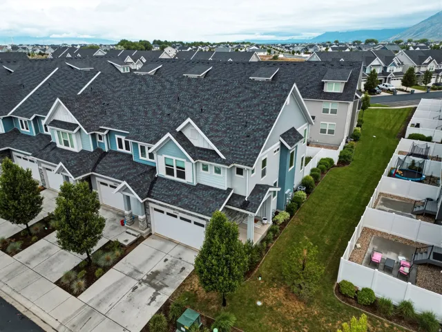 Modern townhome exterior featuring an attached garage, landscaped front yard, stone veneer accents, and a distinctive roofline