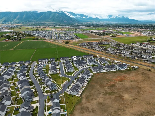 Aerial perspective showcasing a developed residential community with dark-roofed homes, structured street layouts, and surrounding green fields