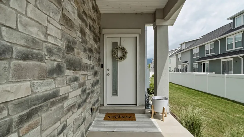 Stone facade entry featuring a white front door with a decorative window, covered porch, and a vinyl privacy fence enclosing a grassy area