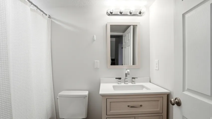 Bathroom featuring a light wood-finish vanity with a white countertop and undermount sink, a framed mirror, and a white toilet