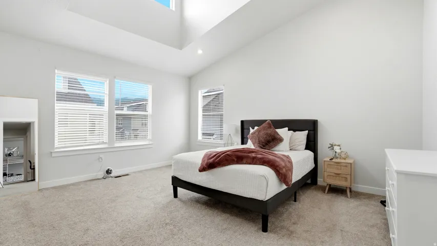 Spacious room featuring vaulted ceilings, a large window array with white blinds, and plush carpeting