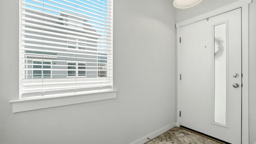 Entryway featuring a white door with a frosted glass panel, a window with horizontal blinds, and stone-finish flooring