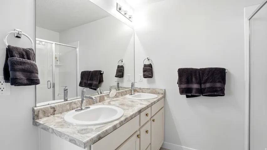 Bathroom featuring a double vanity with integrated sinks, a patterned countertop, and a large wall-mounted mirror