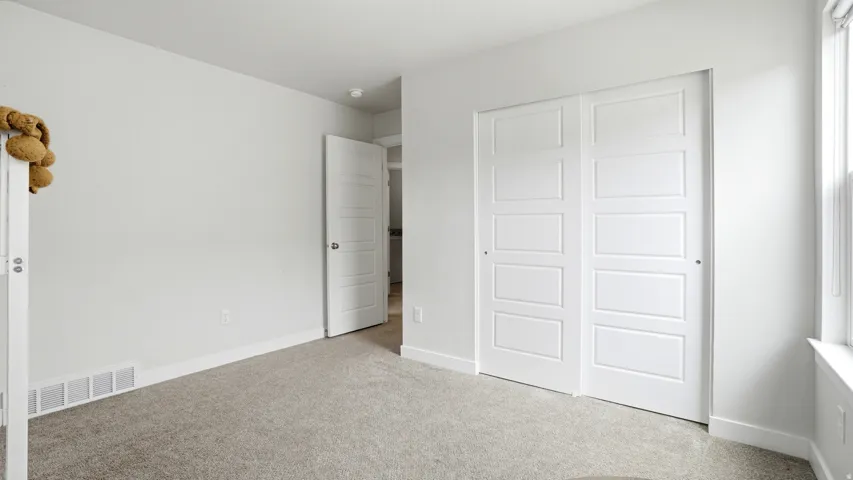 Neutral-toned carpeted room featuring a window, baseboard trim, and white sliding closet doors with recessed paneling