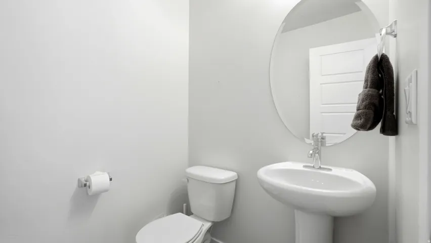 Pedestal sink with a polished chrome faucet, round wall-mounted mirror, and white panel door