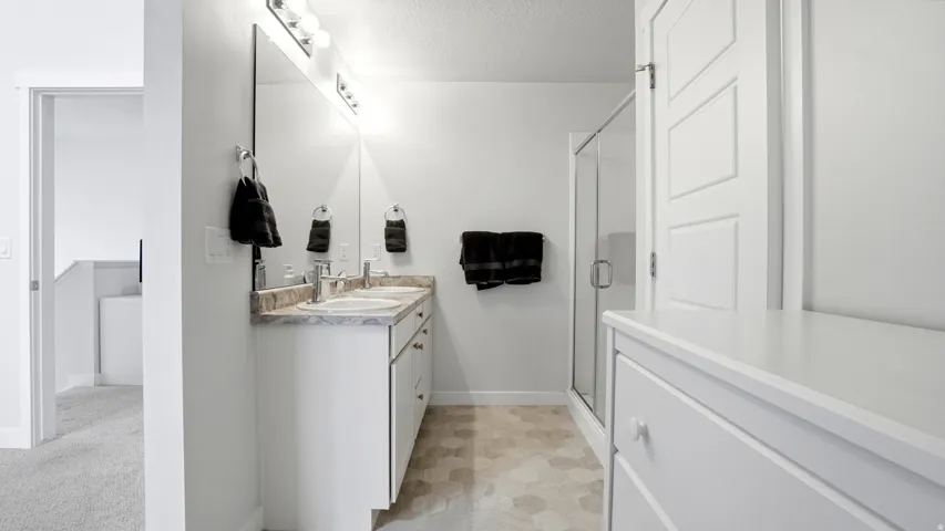 Bathroom featuring a double vanity with two undermount sinks, a large wall mirror, and a glass-enclosed shower