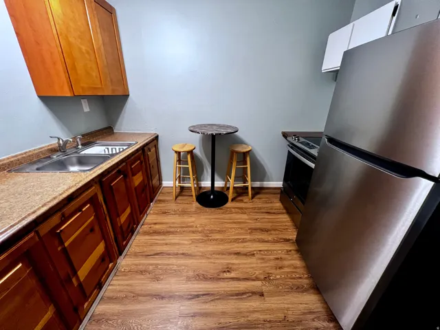 Kitchen featuring wood-finish flooring, full-size stainless steel refrigerator, black range, dual basin stainless steel sink, and wood cabinetry