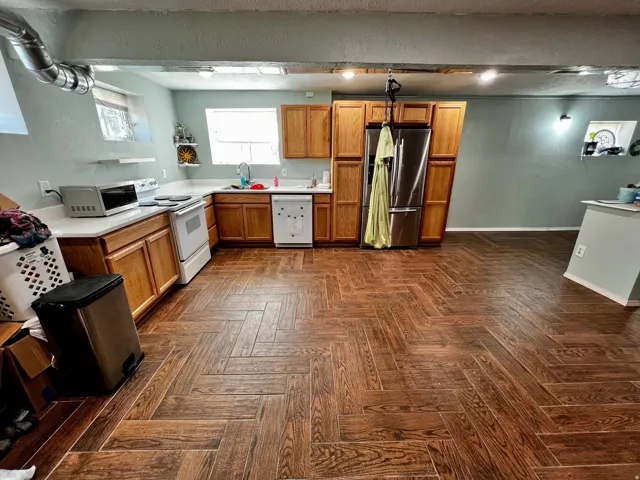 Spacious kitchen featuring a large herringbone wood-finish floor, light wood cabinetry, white countertops, and a stainless steel refrigerator