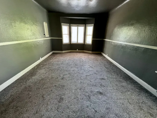 Room featuring bay windows, gray textured carpet, and a two-tone wall treatment with a white chair rail