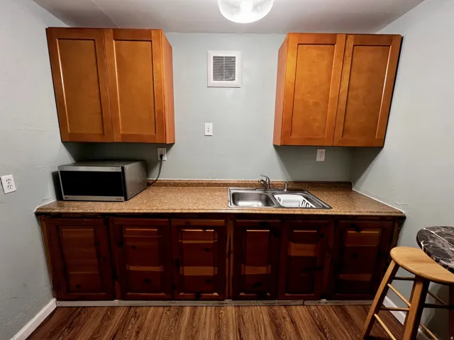 Kitchenette featuring wood-finish flooring, light wood upper cabinetry, darker wood lower cabinetry, and a double-basin stainless steel sink with a chrome faucet