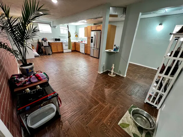 Wood-finish herringbone flooring extending into a kitchen area with light wood cabinetry and stainless steel appliances