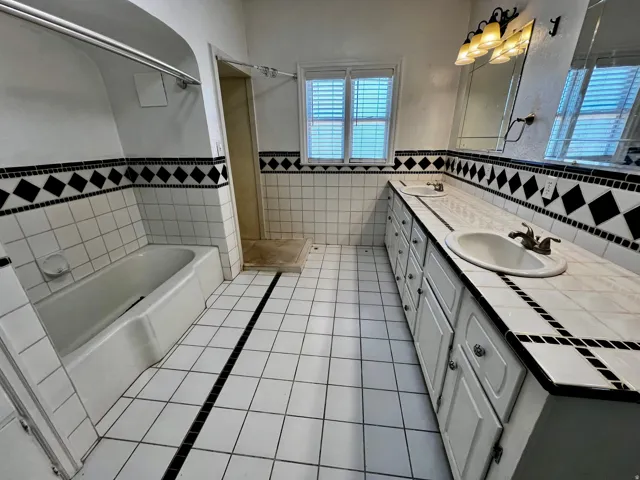 Bathroom featuring a dual vanity with tile countertop, integrated sinks, and under-cabinet storage