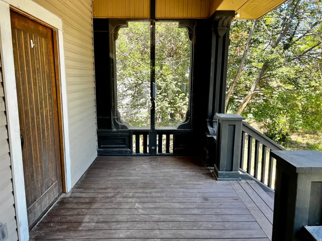 Expansive wooden porch featuring ornate black railings, wood-plank flooring, and a beadboard ceiling