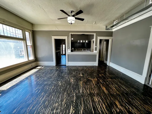 Spacious room featuring dark wood-finish flooring, a contemporary ceiling fan with integrated lighting, and multiple large windows