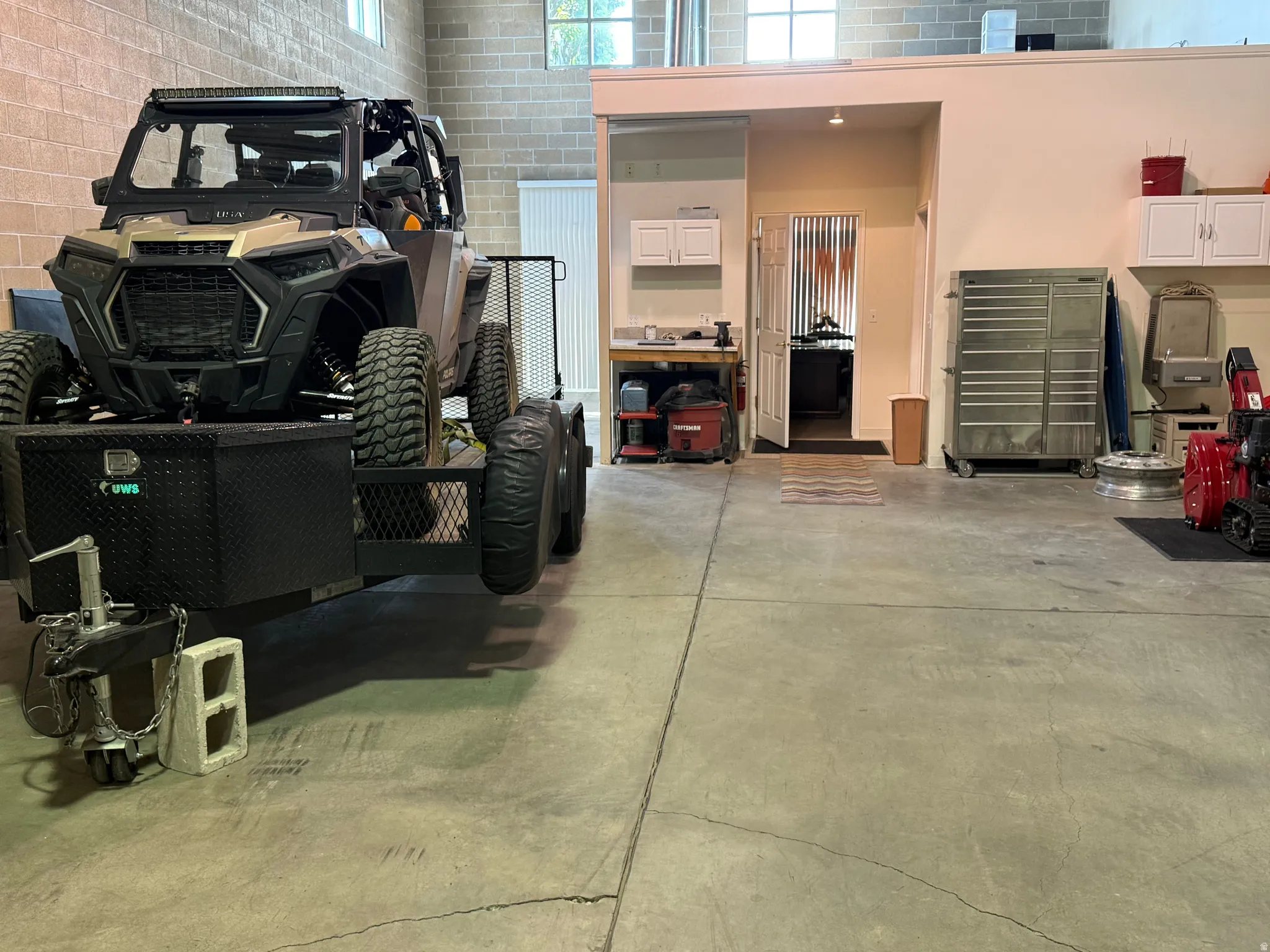Spacious garage featuring a concrete floor, exposed brick walls, and high ceilings with upper windows