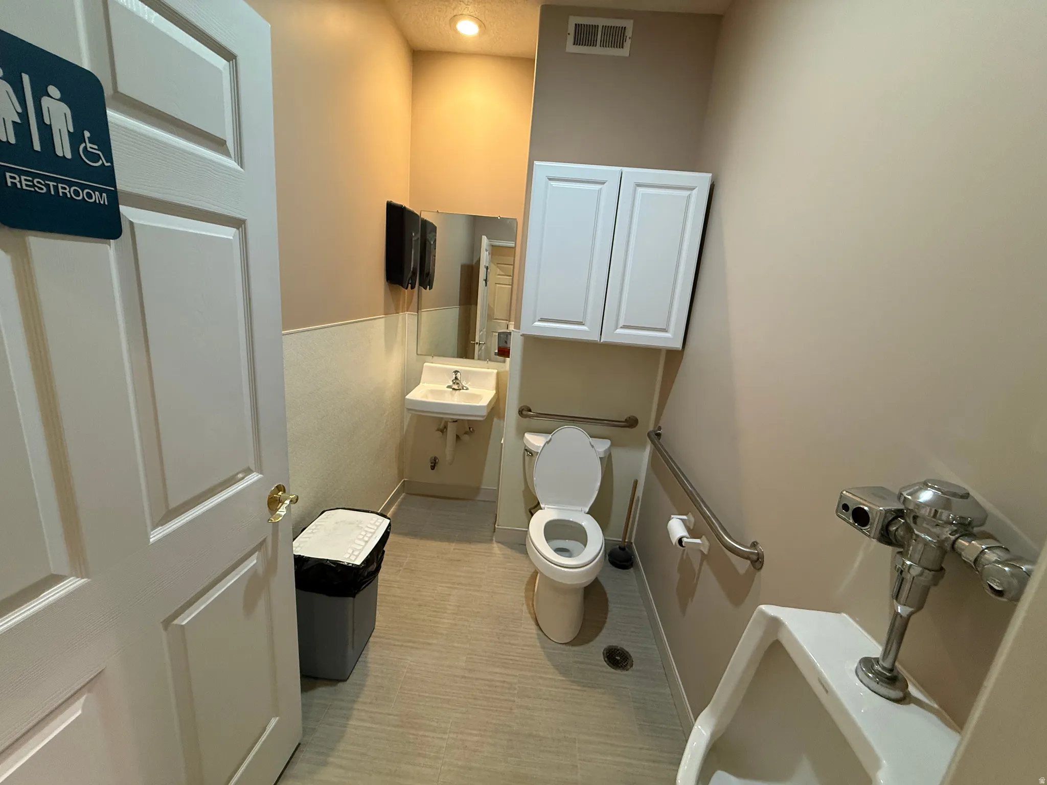 Restroom featuring a wall-mounted sink, toilet with grab bars, and a urinal