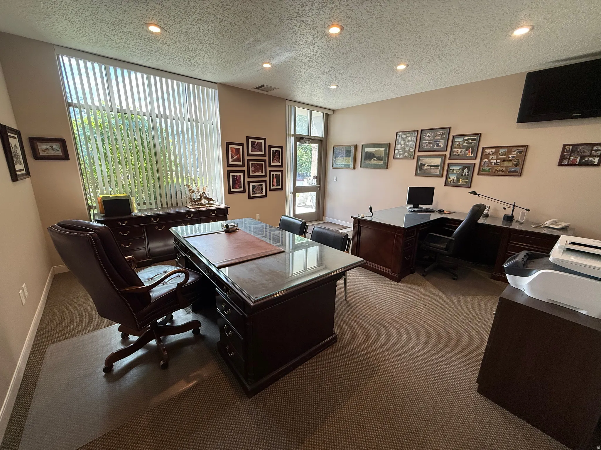 Dedicated office space featuring two dark wood-finish desks with polished surfaces, recessed ceiling lighting, and a large window with vertical blinds
