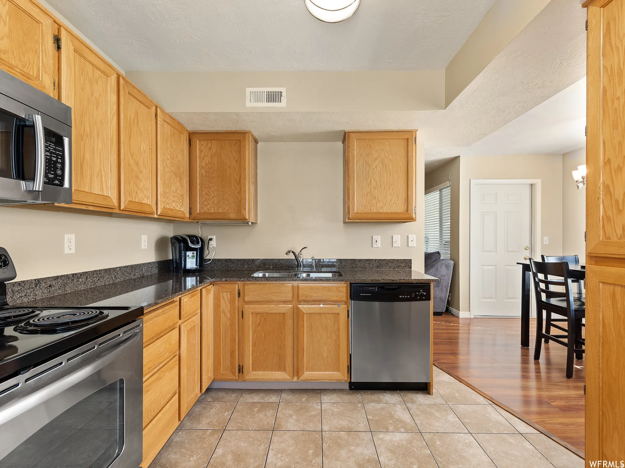 Kitchen featuring wood cabinetry, stainless steel appliances, dark stone-finish countertops, and tiled flooring