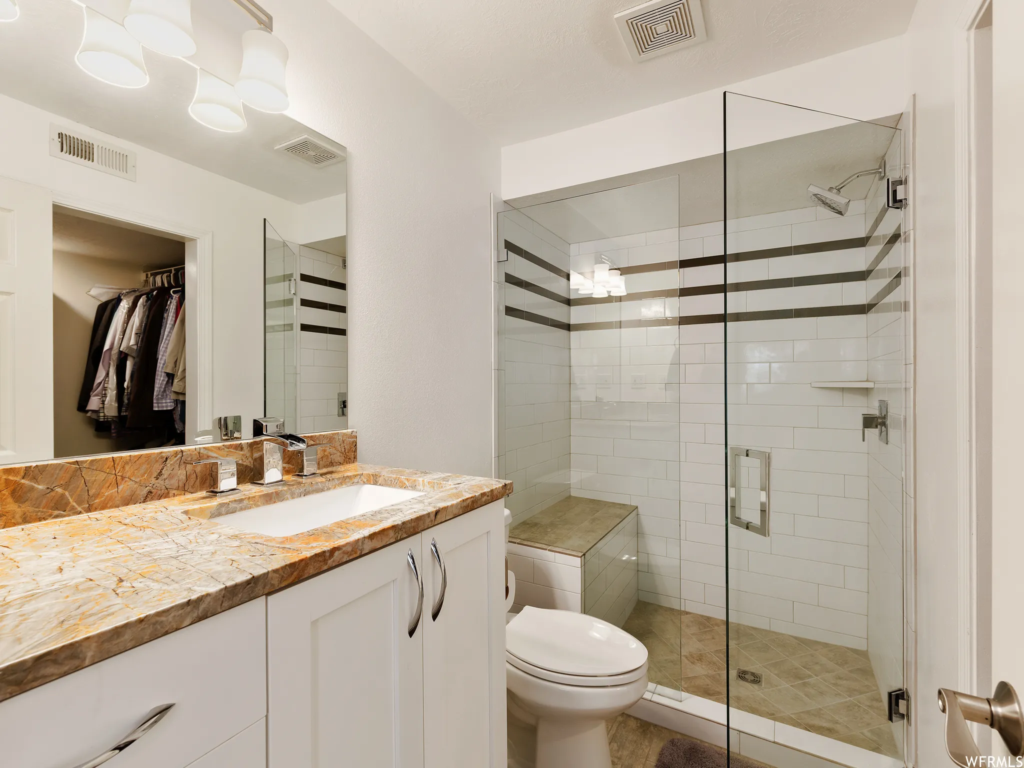 Contemporary bathroom featuring a spacious glass-enclosed shower with subway tile, a built-in shower bench, and a vanity with a stone countertop