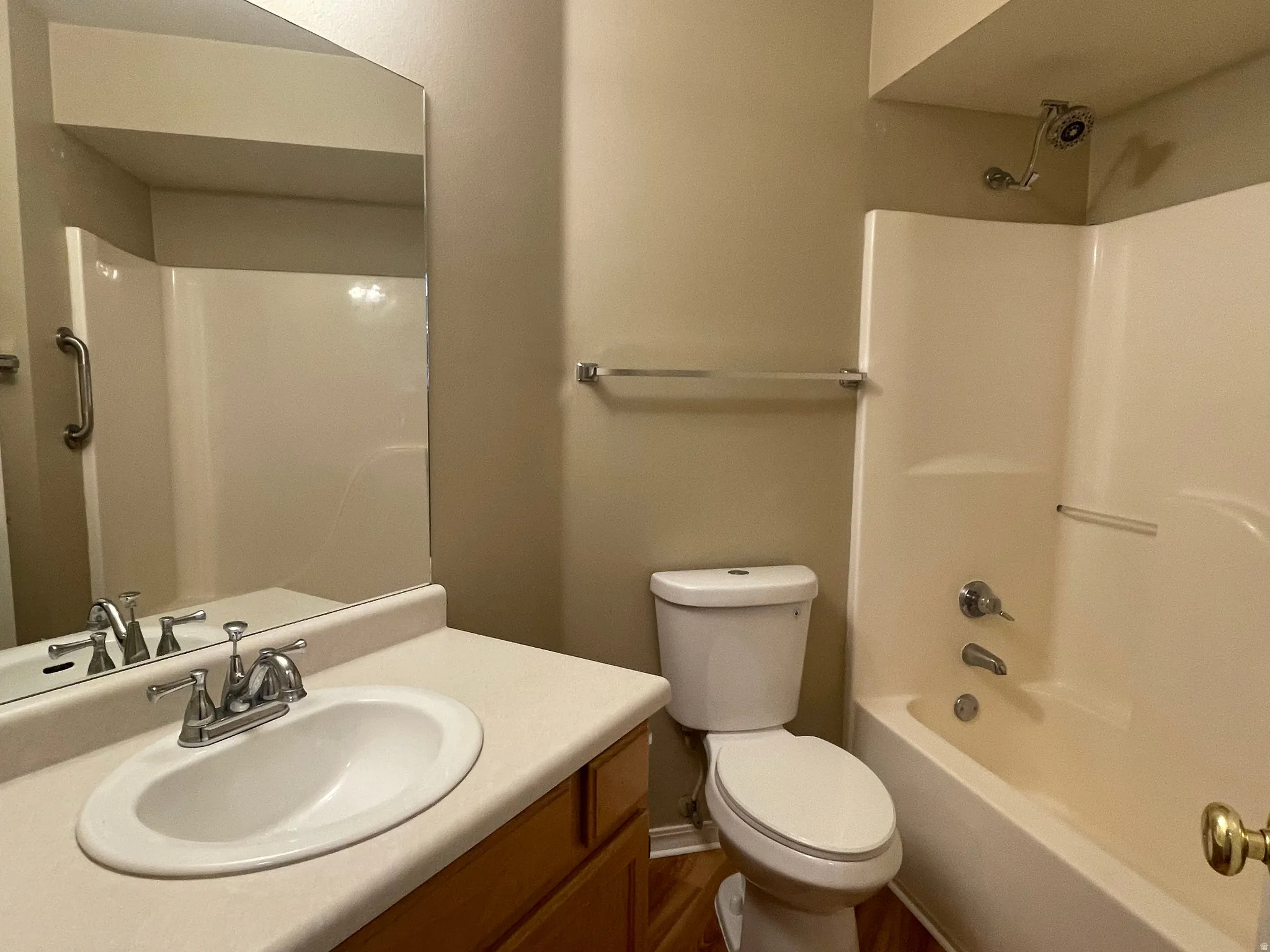 Bathroom featuring a single vanity with an integrated sink, a large wall-mounted mirror, a toilet, a bathtub with an integrated shower, and wood-finish flooring