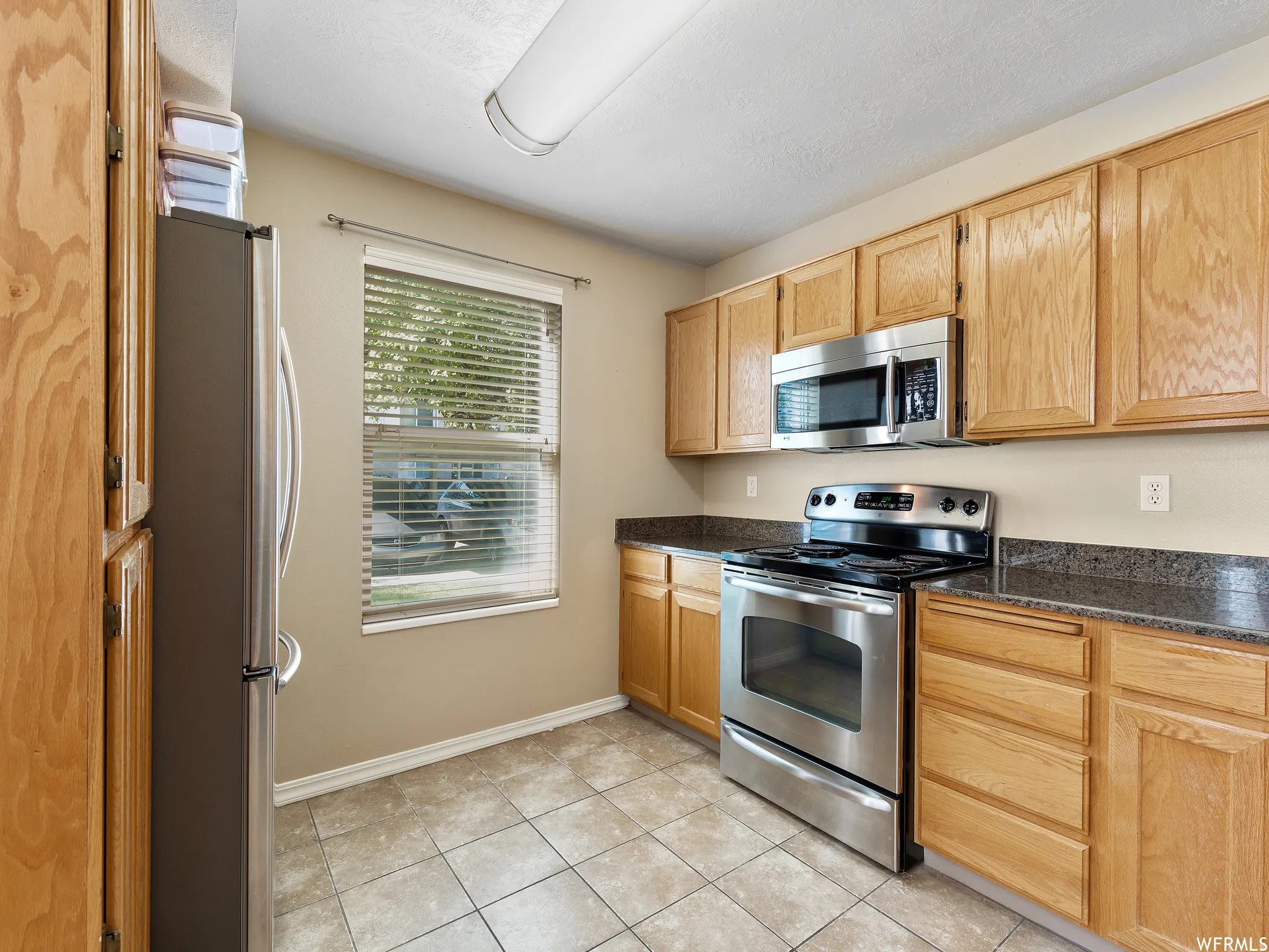 Kitchen featuring wood cabinetry, stainless steel range with overhead microwave, granite-finish countertops, and tile flooring