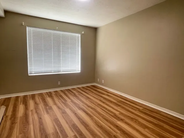 Room featuring wood-finish flooring, a window with horizontal blinds, neutral wall paint, and white baseboards