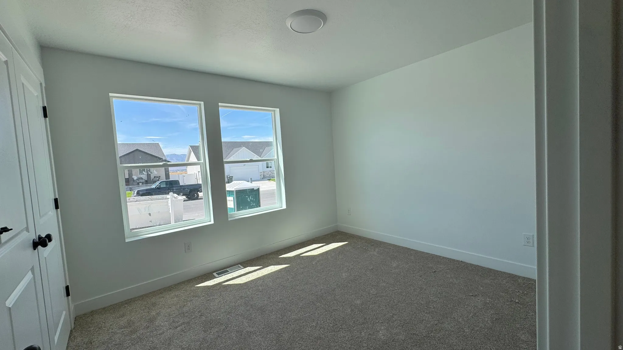Neutral wall colors, carpet flooring, two windows, and a flush mount ceiling light