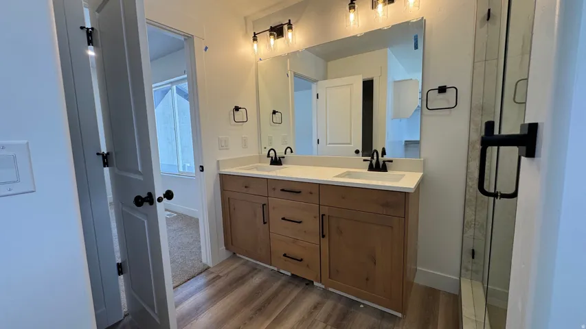 Dual vanity with wood-finish cabinetry, white countertops, and matte black fixtures