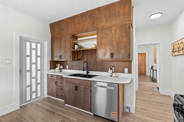 Kitchen featuring wood-finish cabinetry, solid surface countertops, a black double basin sink with a matte black faucet, and a stainless steel dishwasher