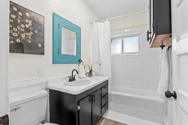 Bathroom featuring a vanity with a white countertop and black cabinetry, a medicine cabinet with a turquoise frame, a toilet, and a bathtub with white subway tile surround