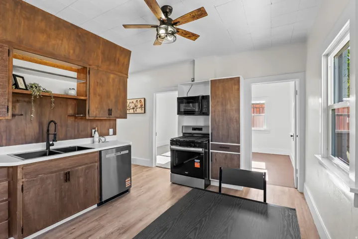 Kitchen featuring wood-finish cabinetry, white countertops, a double basin sink with a matte black faucet, and stainless steel appliances including a range and dishwasher