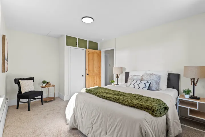 Carpeted bedroom featuring a flush-mount ceiling light, white walls, and built-in upper cabinetry with green doors