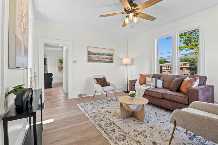 Bright living area featuring wood-finish flooring, white trim, and a ceiling fan with integrated lighting
