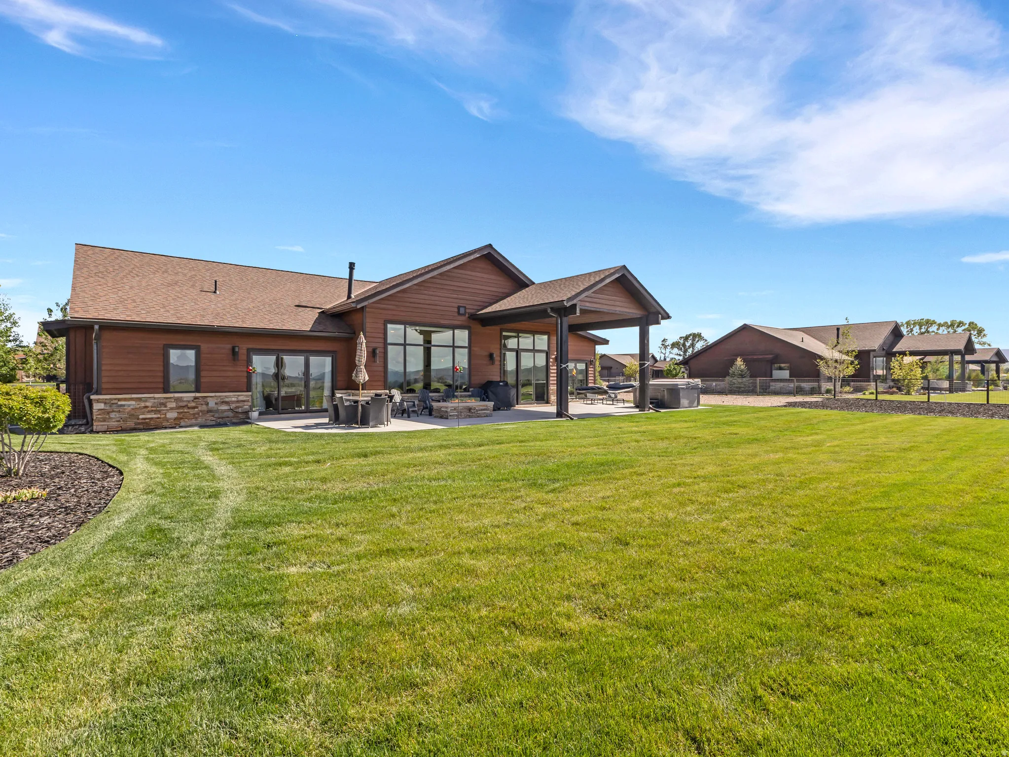 Expansive green lawn with a brown-sided house featuring a stone facade and a covered patio