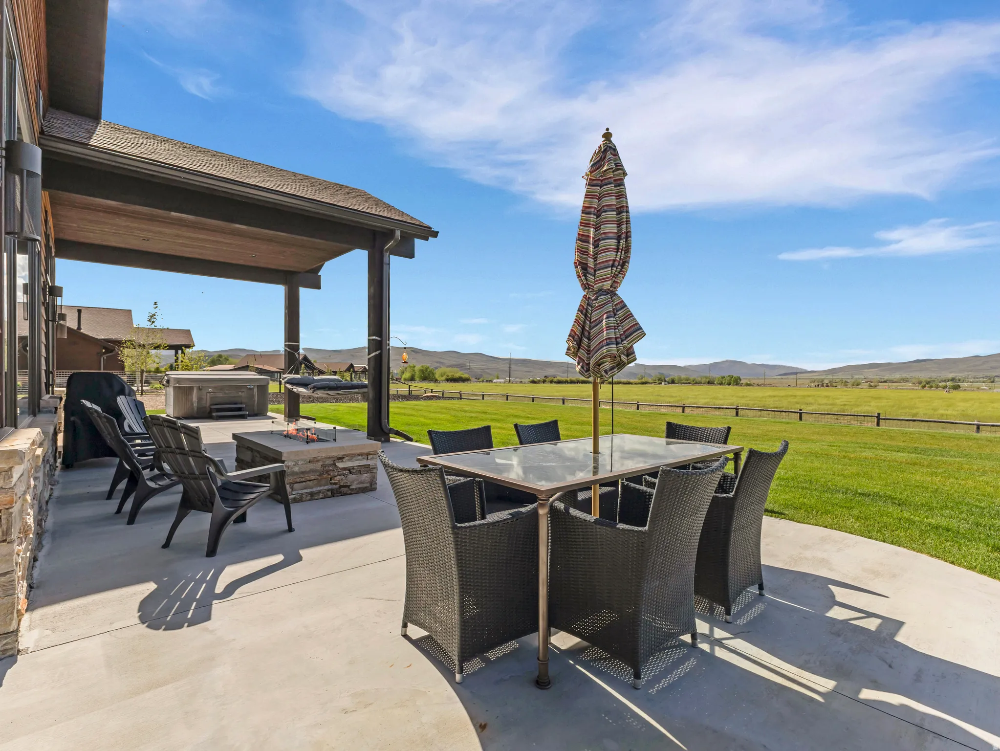 Expansive concrete patio featuring a stone-clad fire pit, covered outdoor living space, and a hot tub