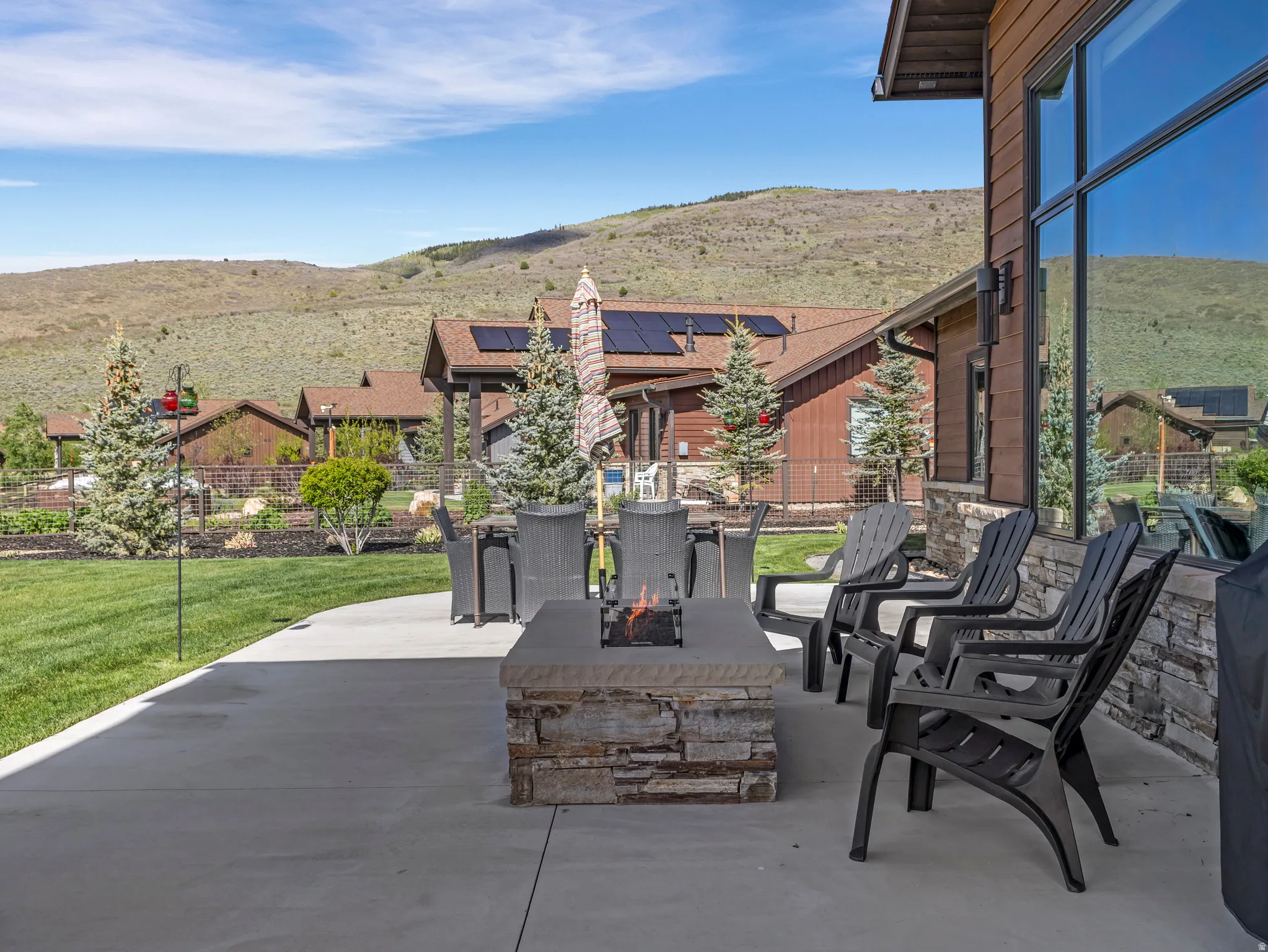 Spacious concrete patio featuring a stacked stone fire pit, extensive lawn area, and mature evergreen landscaping