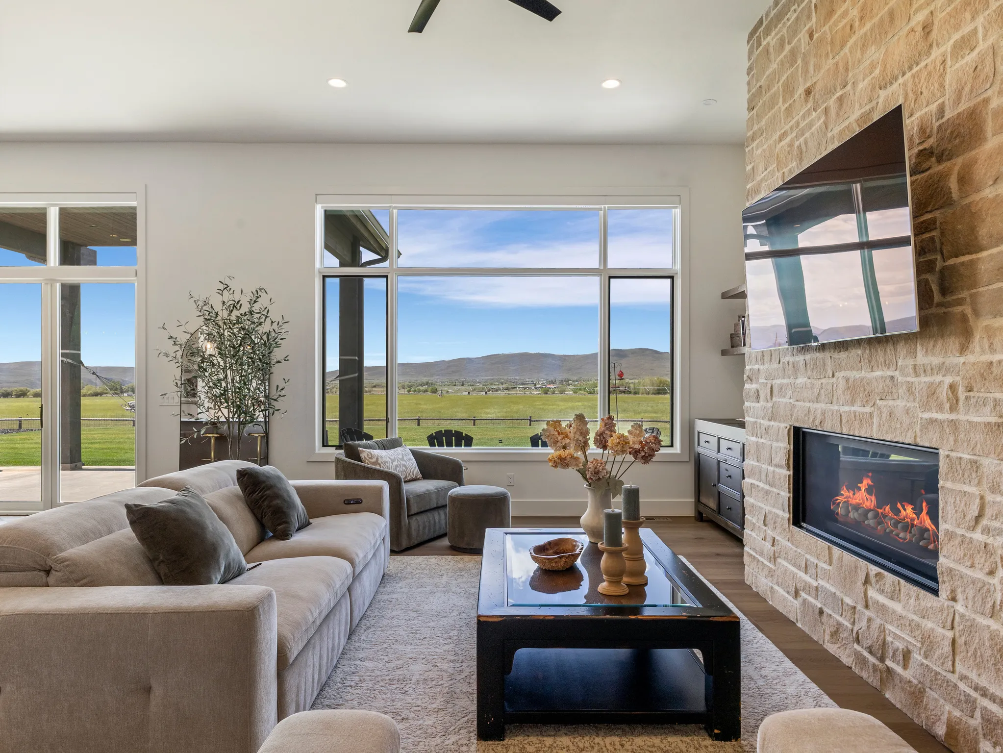 Living area featuring a floor-to-ceiling stone fireplace, expansive windows, sliding glass doors, a built-in linear fireplace, and wood-finish flooring