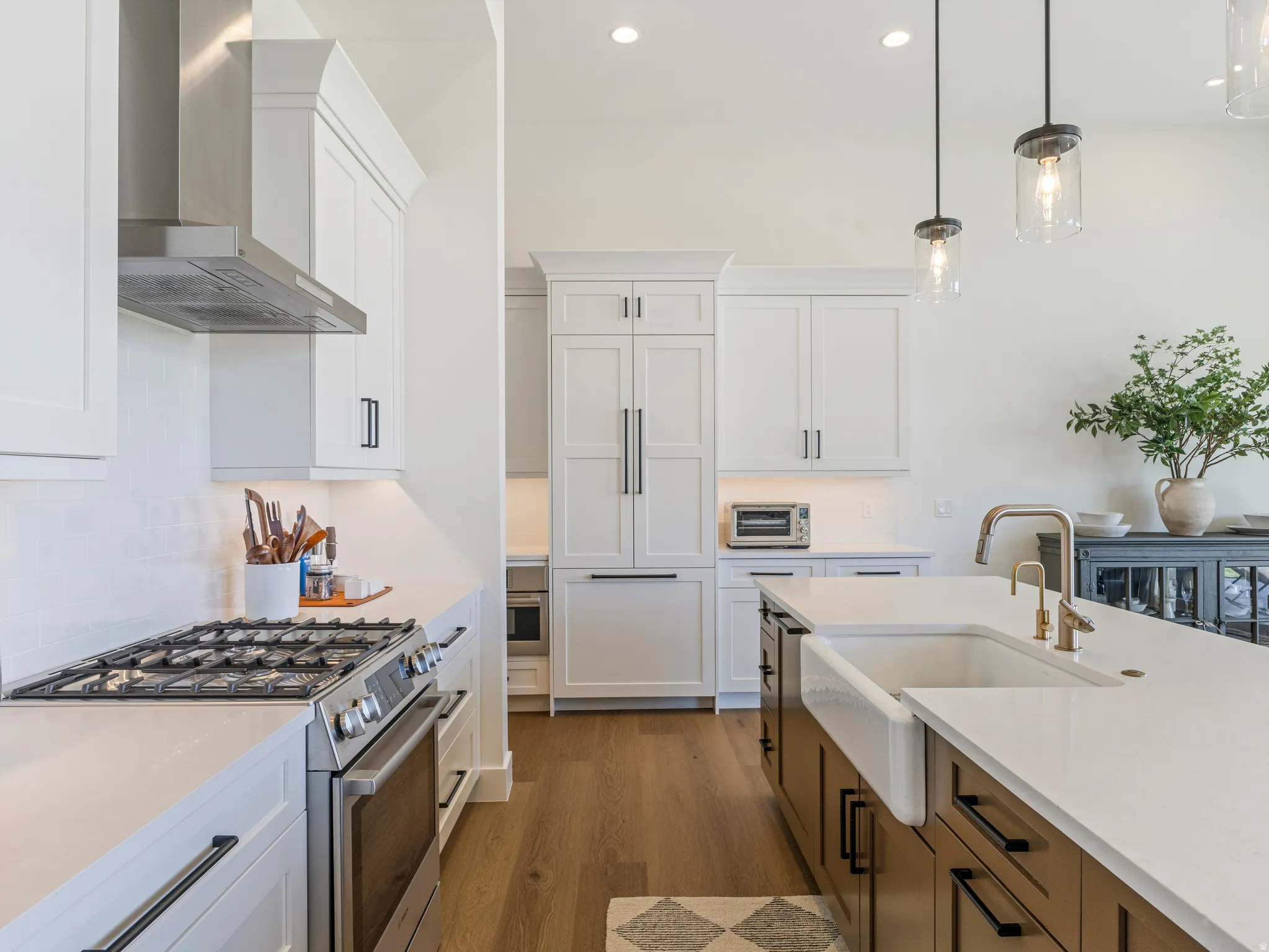 Contemporary kitchen featuring white shaker cabinetry, stainless steel appliances, a farmhouse sink, light wood-finish flooring, and pendant lighting
