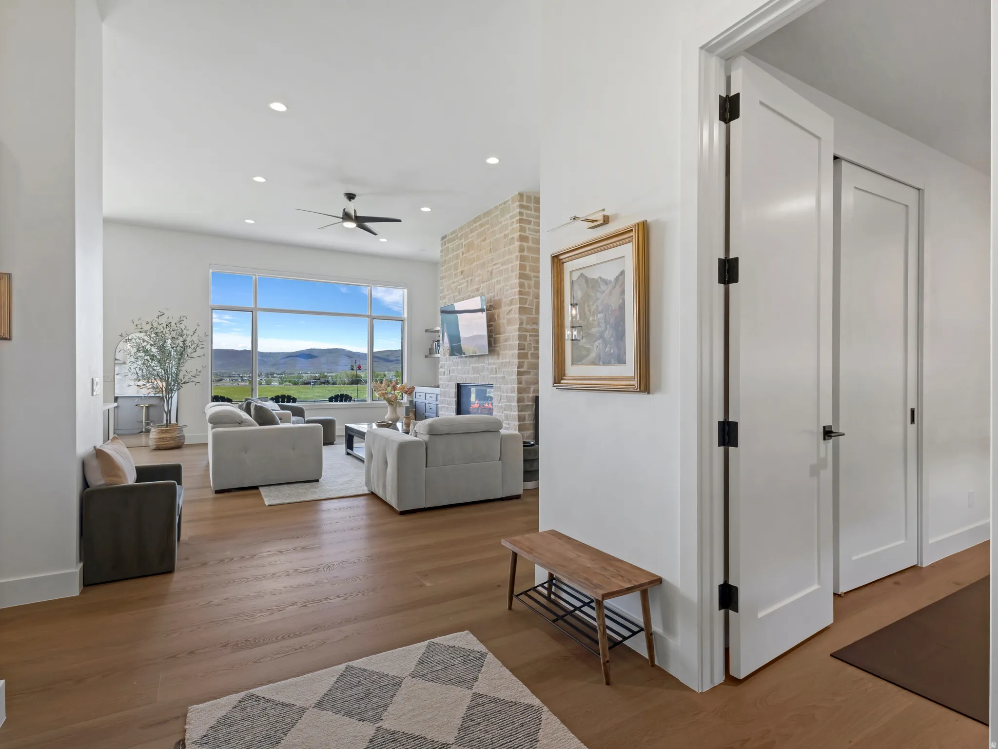 Spacious living area featuring expansive windows, wood-finish flooring, a stone-clad fireplace, recessed lighting, and a contemporary ceiling fan