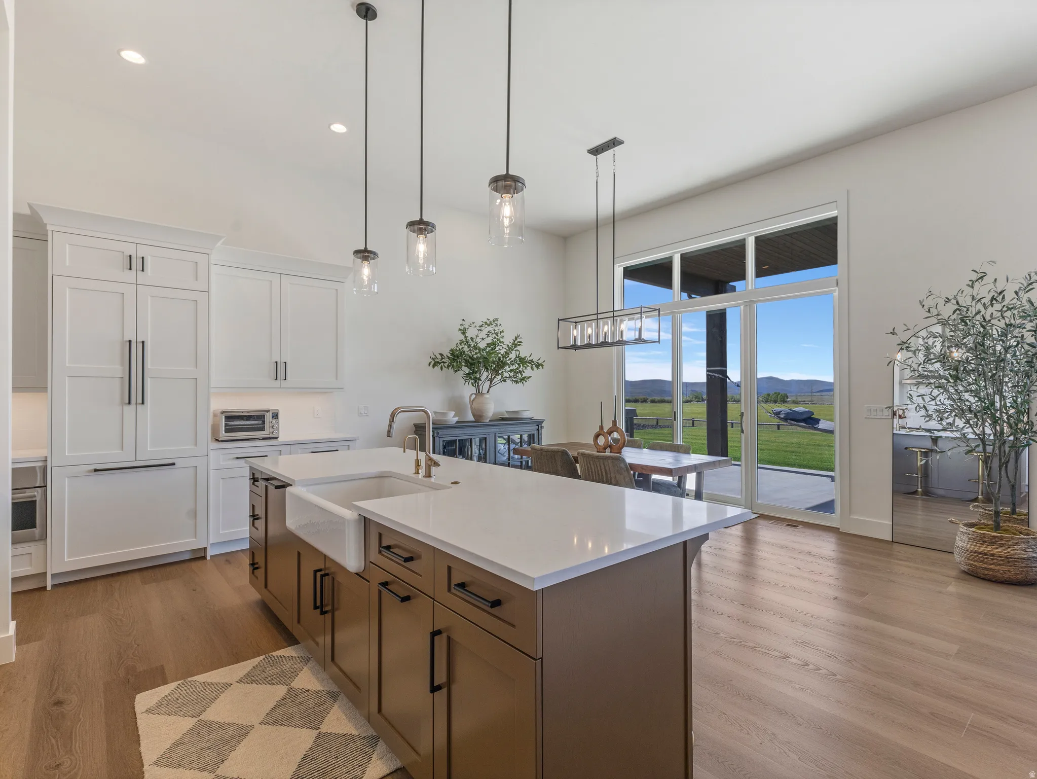 Open-concept kitchen and dining area featuring a large center island with a farmhouse sink and quartz countertop, integrated refrigerator, pendant lighting, and wood-finish flooring