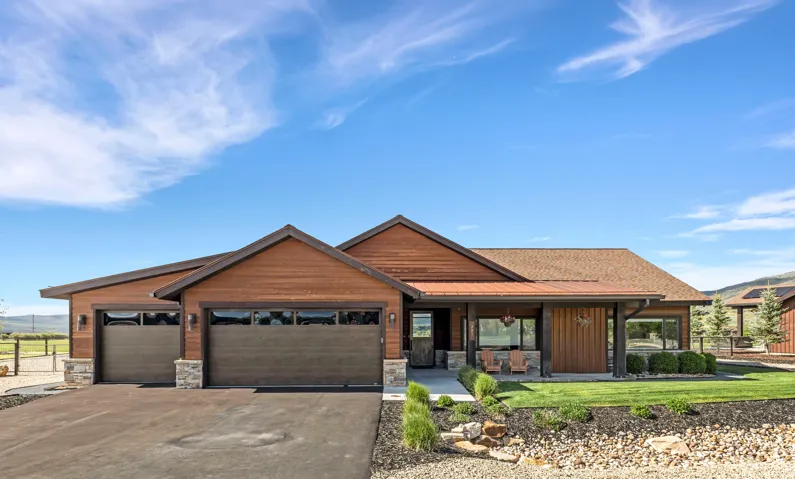 Contemporary ranch-style exterior featuring horizontal wood siding, a two-car garage with frosted glass panels, stone accents on the garage pillars and foundation, a covered front porch with recessed lighting, and a composite shingle roof