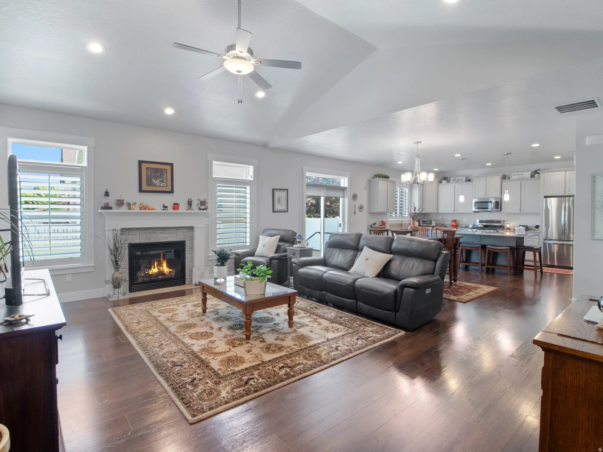 Open-concept living area featuring rich wood-finish flooring, a contemporary fireplace with a tile surround and substantial mantel, and recessed lighting