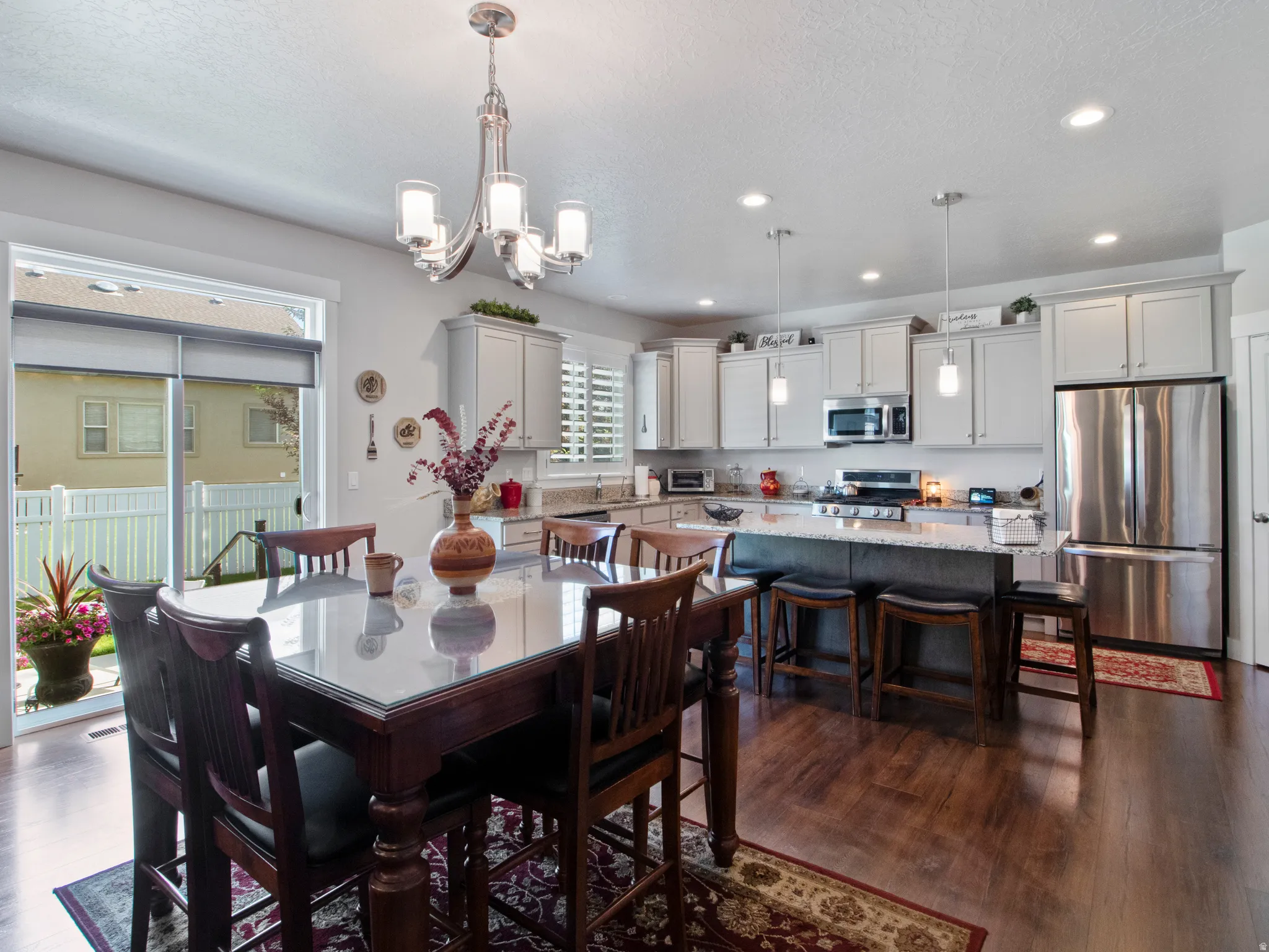 Open-concept kitchen and dining area featuring wood-finish flooring, light gray cabinetry, stainless steel appliances, a center island with bar seating, and a sliding glass door to the exterior