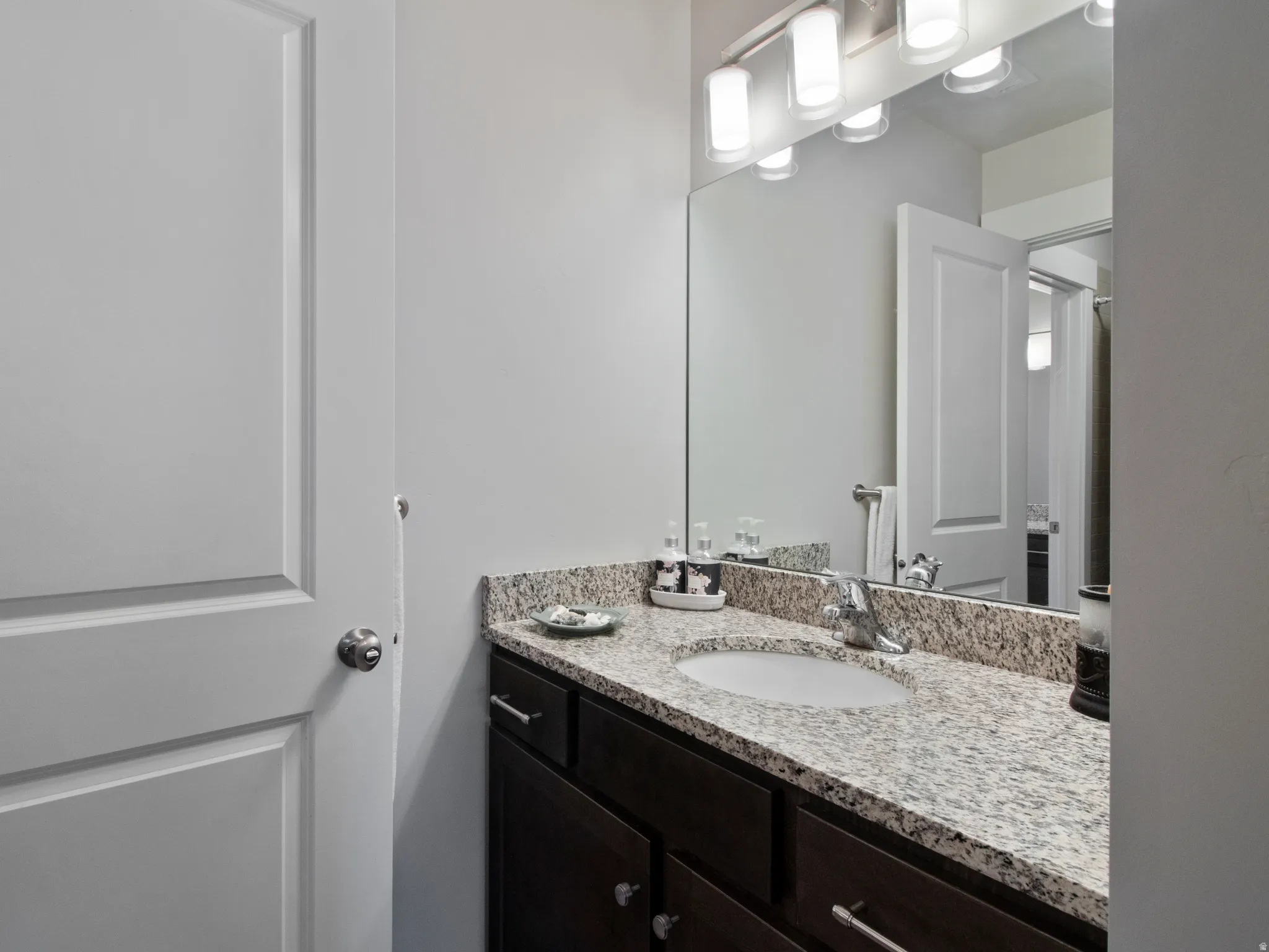 Bathroom vanity featuring a speckled countertop, undermount sink, and dark wood cabinetry with chrome hardware